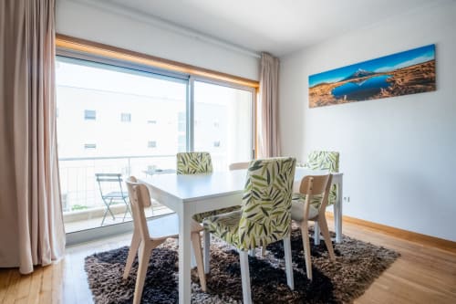 Modernes Esszimmer im EcoHost Arcozelo mit weißem Tisch, gemusterten Stühlen, Balkonaussicht und Landschaftskunst