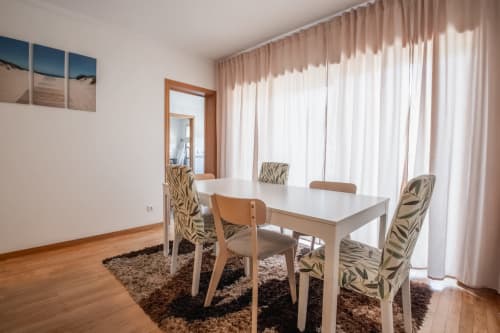 Modernes Esszimmer mit weißem Tisch, gemusterten Stühlen und raumhohen Vorhängen mit Balkonblick im EcoHost