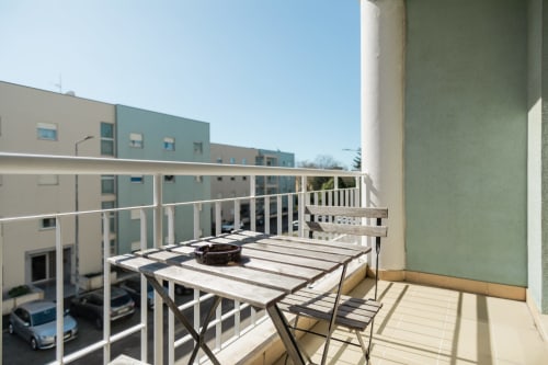 Sonniger Balkon des EcoHost-Apartments in Arcozelo mit Esstisch, weißem Geländer und Blick auf Grünflächen