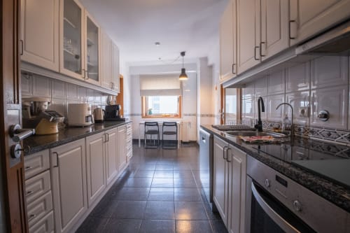 Moderne Küche im Apartment Arcozelo mit cremefarbenen Schränken, dunklen Arbeitsplatten, Edelstahlgeräten und natürlichem Licht