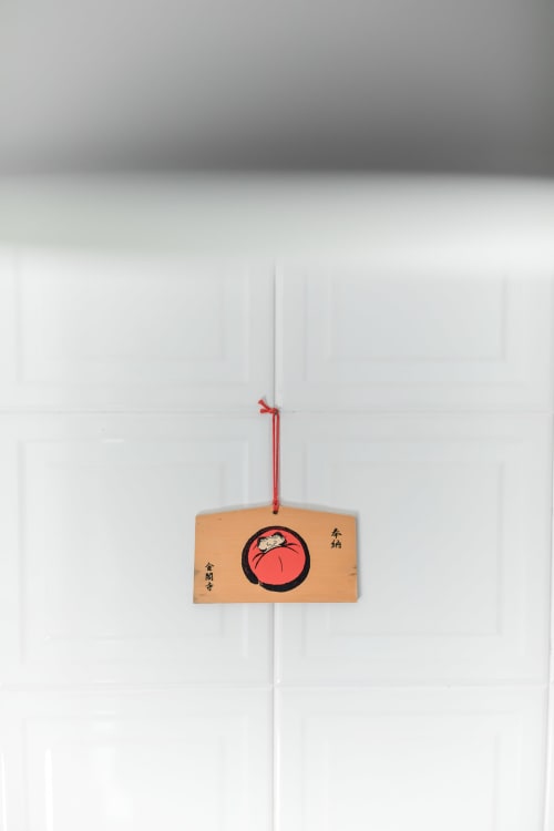 Japanischer Holzschmuck mit rotem Kreis und Schriftzeichen an roter Schnur an weißer Wand aufgehängt