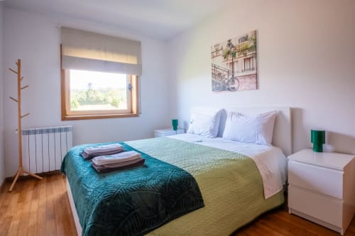 Helles Schlafzimmer im EcoHost Arcozelo mit Queensize-Bett, türkisblauen Bettwäschen, Holzböden, großem Fenster mit Grünblick