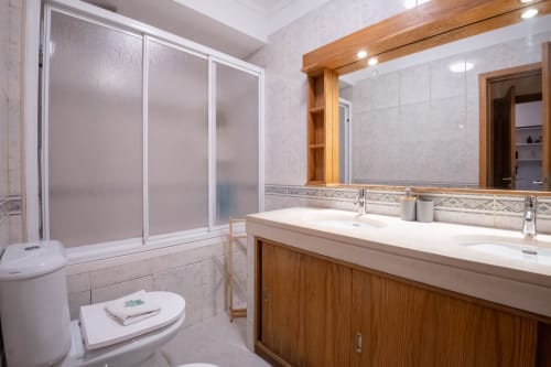 Modernes Badezimmer mit Doppelwaschbecken, Holzwaschtisc, großem Spiegel und Glasduschkabine im EcoHost Gaia Beach&Golf