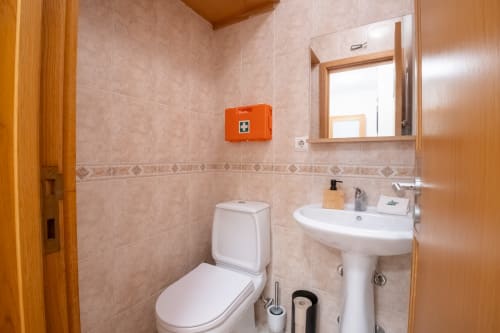 Modernes Badezimmer im EcoHost Gaia Beach&Golf mit weißem Waschbecken, Toilette, Spiegel und orangefarbenem Erste-Hilfe-Kasten in Arcozelo