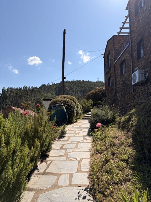 Caminho de pedra em jardins paisagísticos da Casas do Sinhel, com vistas para a montanha e floresta ao fundo