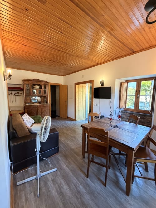 Interior da Casa Relva da Mó com teto de madeira, mesa de jantar, sala de estar, TV e vistas para a montanha