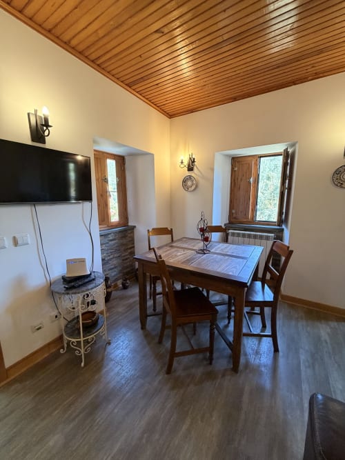 Sala de refeições da cottage Casa Relva da Mó com mesa de madeira, cadeiras, TV e vistas para as montanhas através das janelas