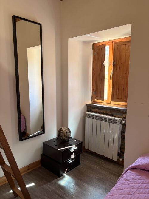 Quarto moderno da Casa Sinhel com espelho preto, criado, guarda-roupa de madeira, radiador e portas com vista para montanha