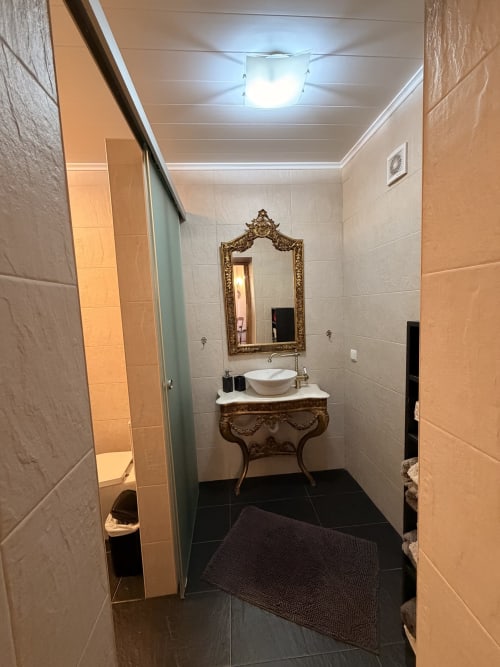 Banheiro elegante na Casa Relva da Mó com espelho moldura dourada, cuba esculpida, piso em azulejos pretos e tons creme
