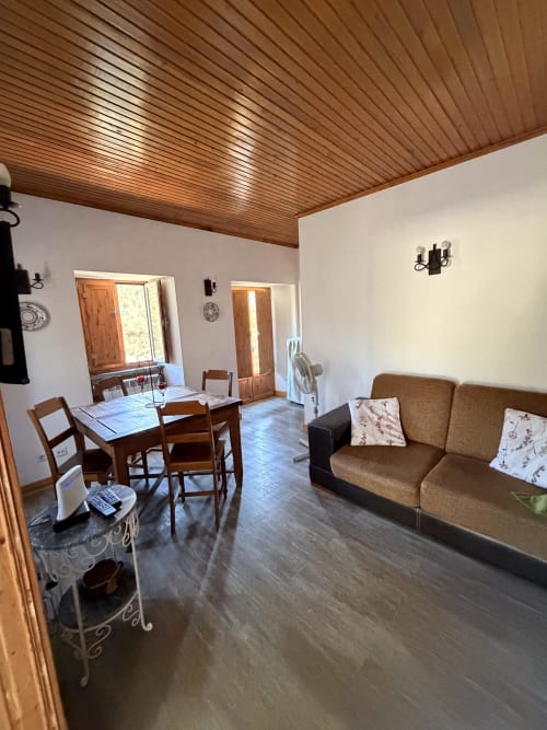 Área clara de estar e refeições em Casa Relva da Mó com teto de madeira, sofá marrom, mesa de jantar e vistas para a montanha