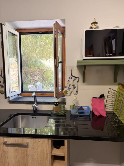 Cozinha moderna com bancada preta, pia de aço inoxidável e janela aberta com vista para o jardim da quinta Casas do Sinhel