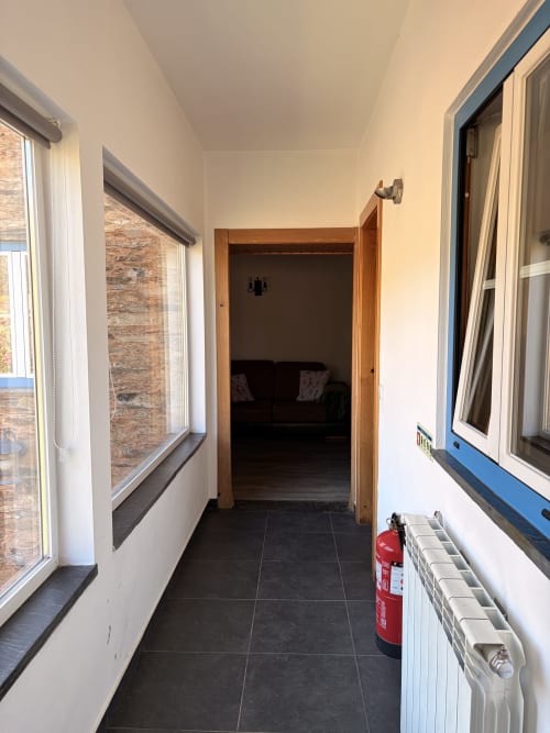 Corredor luminoso da casa de hóspedes Casa Relva da Mó com piso de azulejos escuros, janelas, porta de madeira, radiador e extintor