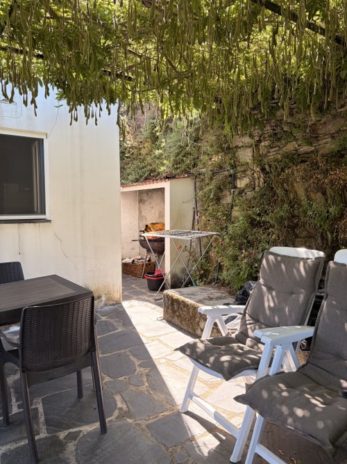 Pátio da cottage em Casas do Sinhel com espreguiçadeiras, mesa de jantar e paredes cobertas de vegetação criando um refúgio ao ar livre