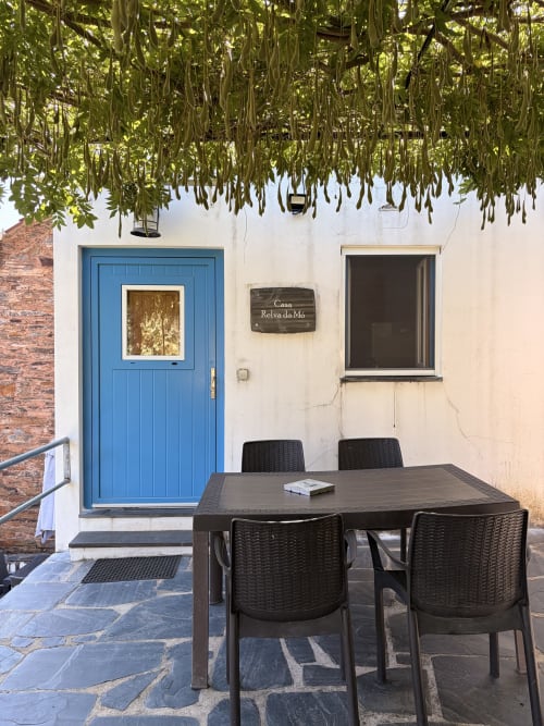 Pátio da Casa Relva da Mó com porta azul, mesa de jantar e plantas suspensas em Relva da Mó, Portugal