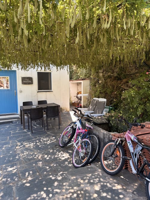Pátio tranquilo das Casas do Sinhel com bicicletas, mesa de jantar e glicínias em cascata acima