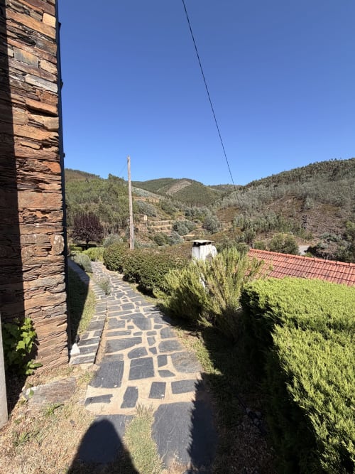 Caminho do alojamento em Casas do Sinhel com entrada de pedra, jardins e montanhas florestadas em Portugal