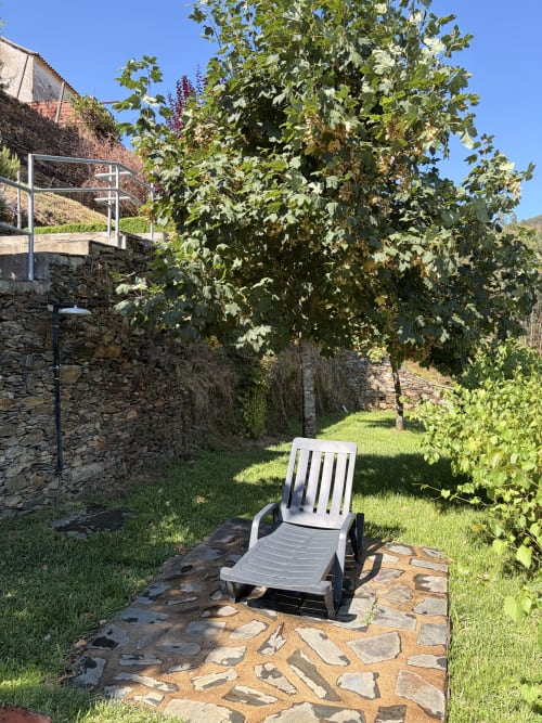 Cadeira espreguiçadeira branca no pátio de pedra em jardim exuberante da casa de hóspedes Casas do Sinhel com vista para as montanhas