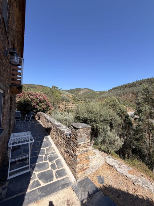 Terraço com vista para a montanha na casa de turismo Casa da Adega em Casas do Sinhel, Portugal, com pátio em pedra e plantas com flores rosa
