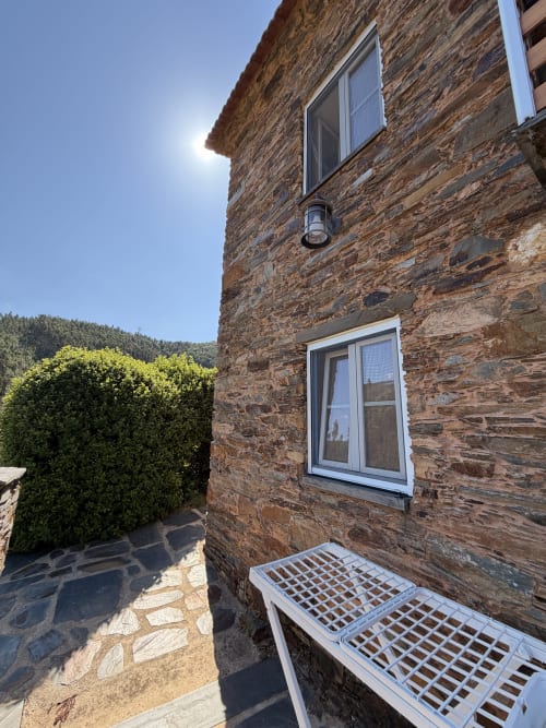 Exterior de casa de pedra em Casas do Sinhel com janelas brancas, vista das montanhas e jardim com cercas aparadas