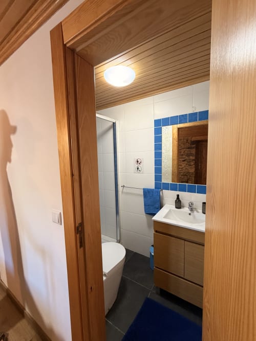Banheiro moderno da casa de hóspedes Casas do Sinhel com azulejos branco e azul, armário em madeira, chuveiro e vaso sanitário