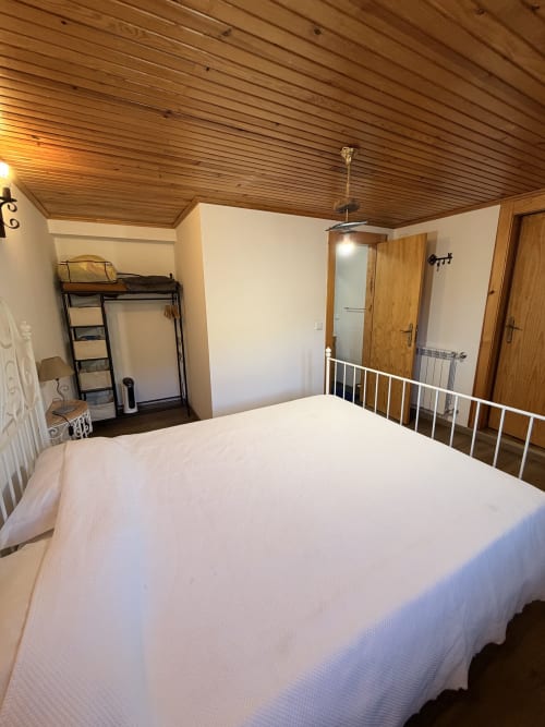 Quarto espaçoso na casa rural Casas do Sinhel com cama de ferro branca, teto de madeira, sótão e entrada para casa de banho