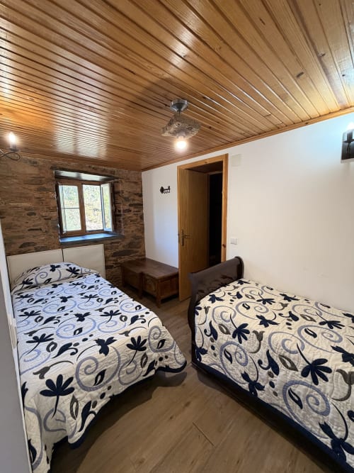 Quarto na casa rural Casa da Adega com duas camas, teto de madeira, paredes de pedra e vista para as montanhas pela janela