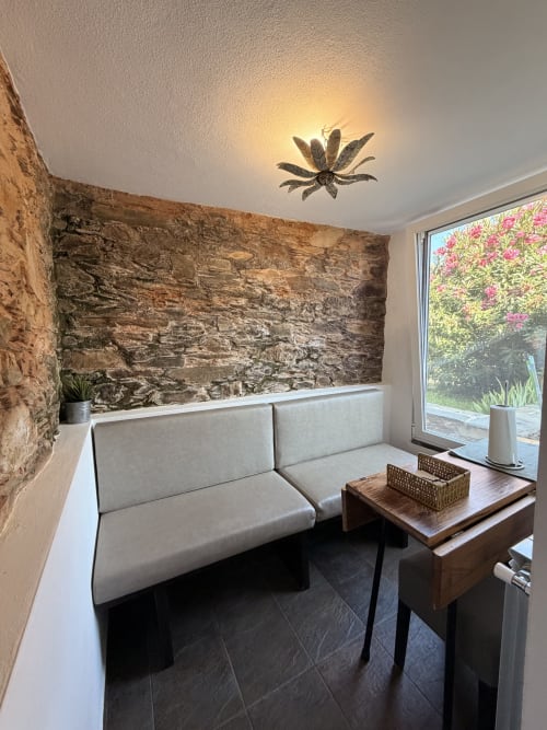 Área de estar moderna na Casas do Sinhel com parede de pedra, móveis cinzentos, mesa de madeira e vista para o jardim
