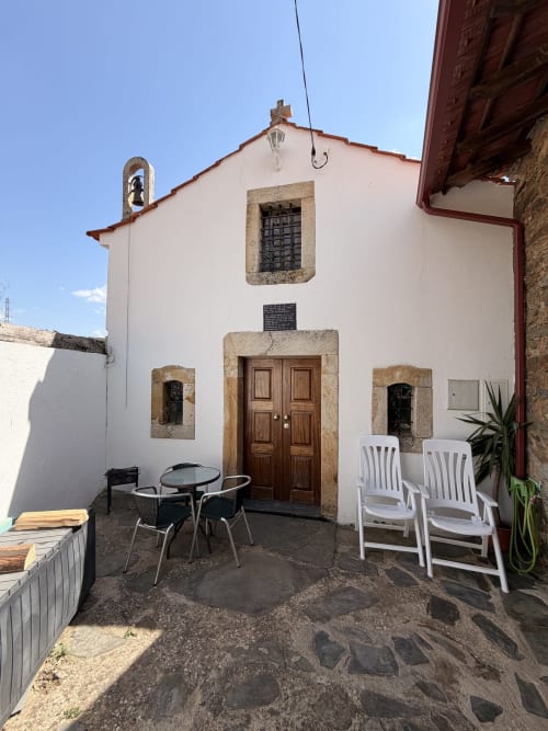 Pátio da vila Casa da Capela com paredes de pedra branca, porta de madeira, área de estar e torre sineira em Casas do Sinhel, Roda