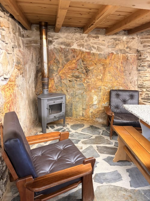 Sala de estar rústica em pedra com lareira, poltronas de couro e vigas de madeira aparente na villa Casas do Sinhel