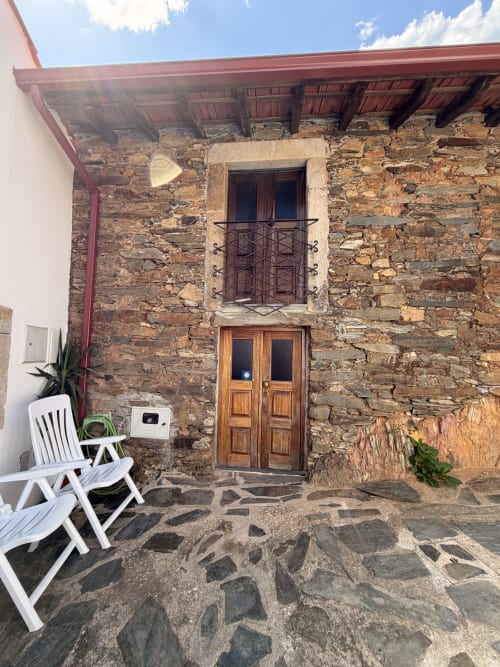 Casarão de pedra com porta de madeira e varanda na vila Casas do Sinhel em Portugal, com área de pátio e cadeira branca