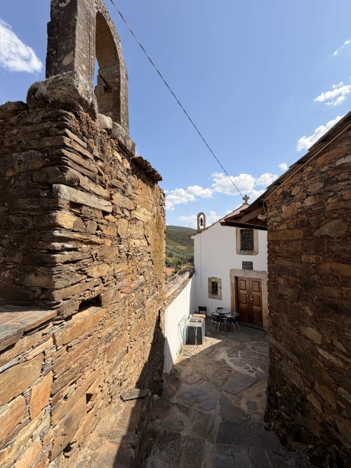 Viela de pedra estreita na vila Casas do Sinhel em Roda Fundeira, Portugal, com capela branca e vistas para as montanhas