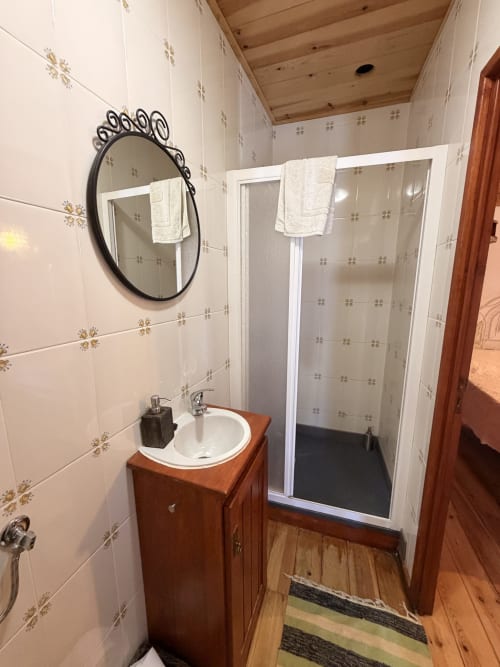 Banheiro moderno com penteadeira de madeira, espelho redondo e box no Casarão Casas do Sinhel em Roda Fundeira, Portugal