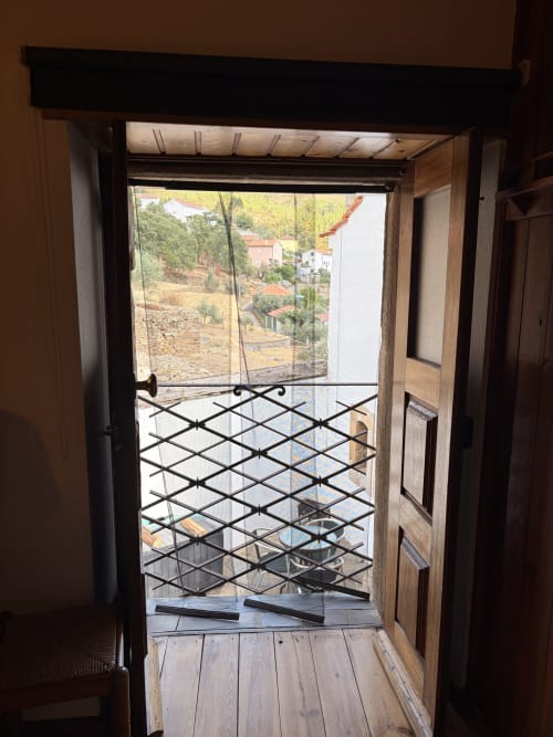 Porta de madeira aberta com corrimão de metal preto na varanda da villa com vista para as montanhas de Roda Fundeira e zona rural em Casas do