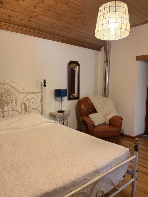 Quarto elegante na villa Casas do Sinhel com cama ornamentada, poltrona de couro, teto de madeira e iluminação moderna