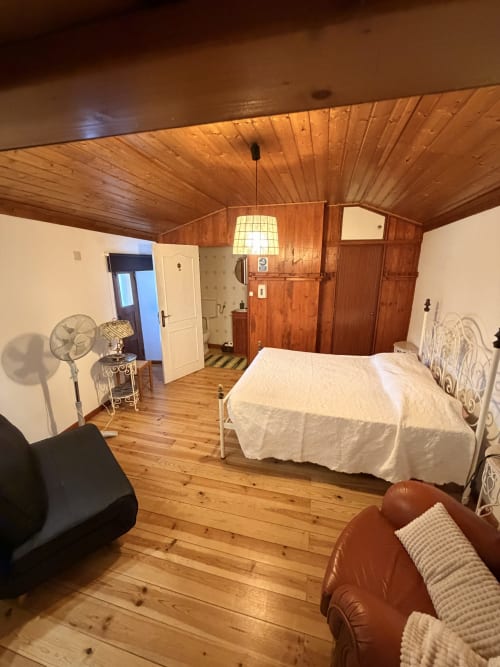 Quarto aconchegante da villa Casas do Sinhel com teto de madeira, cama de ferro branco, móveis em couro e vista para as montanhas