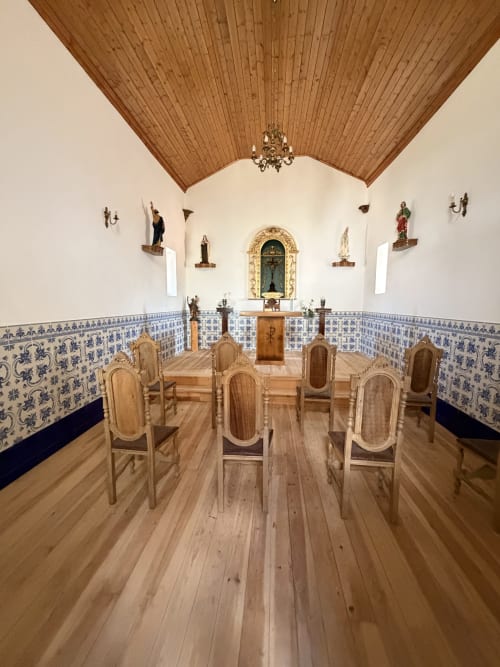 Interior da capela iluminada por velas na quinta Casas do Sinhel com teto de madeira, azulejos azuis nas paredes, altar e cadeiras de madeira