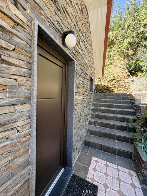 Entrada de porta moderna e escura da quinta Casa das Oliveiras em Alvares, com paredes de pedra e escadas exteriores