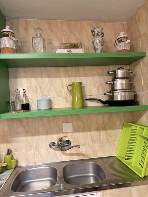 Prateleiras verdes na cozinha da vila Casas do Sinhel com utensílios de cozinha, vasos decorativos e louça acima da pia dupla