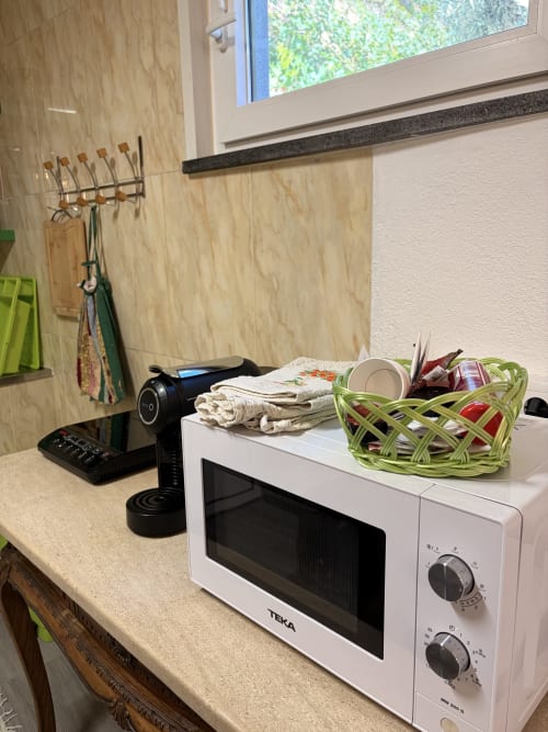 Canto da cozinha na villa Casa das Oliveiras com micro-ondas, cafeteira e cestos de armazenamento próximos à janela com vista para Alvares