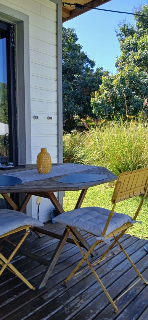 Patio de la villa moderne au Domaine de Jade avec table en bois, chaises moutarde et vue sur le jardin luxuriant à Saint-André