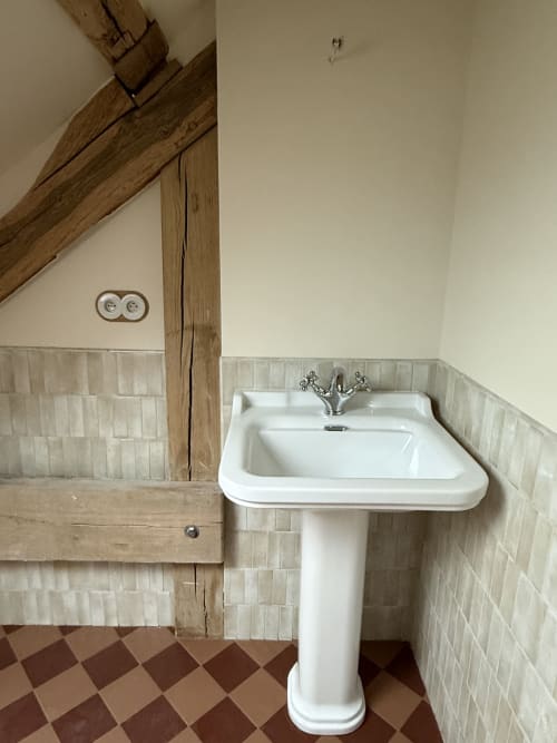 Lavabo sur piédestal avec robinetterie chromée dans la chambre La Rose sauvage à La Grange Aux Etangs, Sennely, aux poutres apparentes