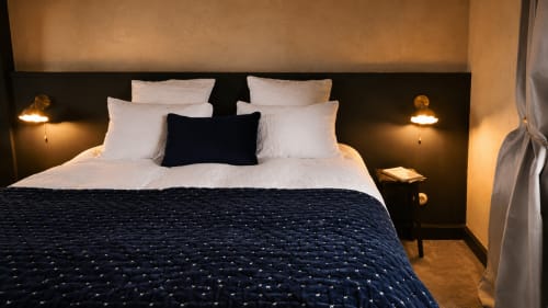 Elegant bedroom at La Maison 1903 in Trévou-Tréguignec with white pillows, dark blue quilted bedding, and warm ambient