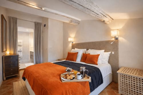 Suite Cezanne bedroom at Les Suites de Montigny, Aix-en-Provence, featuring king bed with orange accents, exposed beams, and