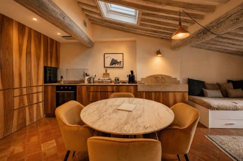 Suite Cezanne at Les Suites de Montigny: open-plan living with round marble table, orange chairs, wood beams, kitchen, and