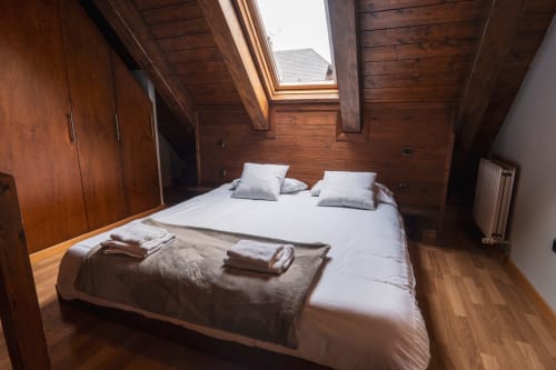 Deluxe Quadruple Room at La Borda del Gato Rafa in Vielha with wooden beams, skylight, and white bedding