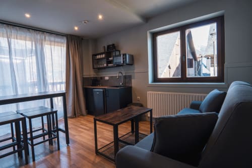 Modern hotel room in Vielha with kitchenette, comfortable seating, wooden floors, and city views from balcony