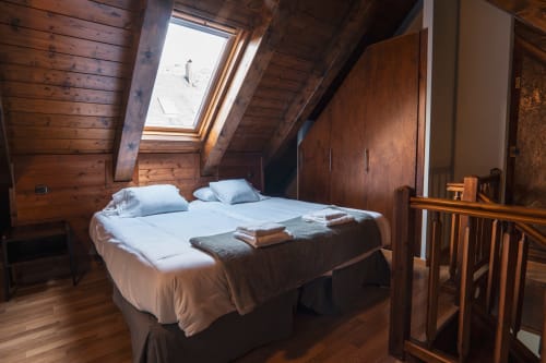 Cozy attic bedroom at La Borda del Gato Rafa in Vielha with wooden beams, skylights, and a bed with white linens