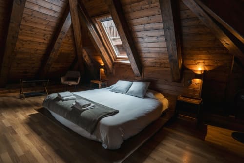 Wooden attic bedroom at La Borda del Gato Rafa in Vielha with queen bed, skylights, wooden beams, and warm lighting