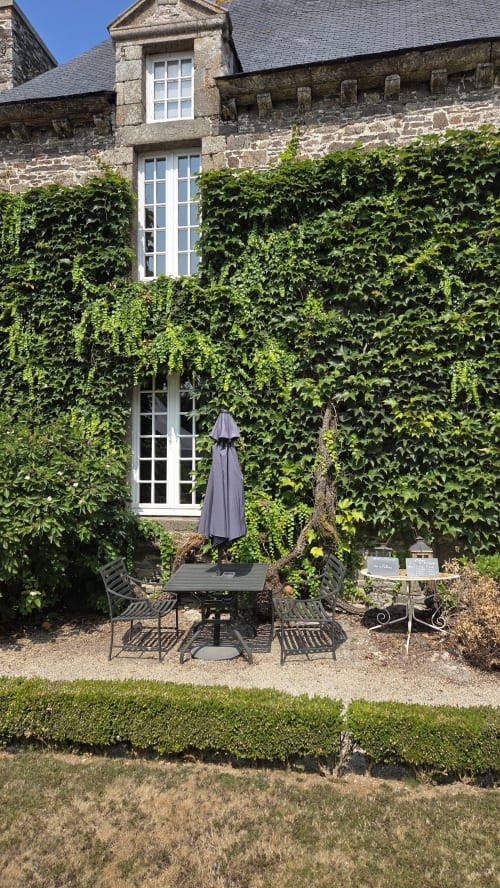 Manoir de pierre aux murs couverts de lierre, terrasse avec parasol et portes-fenêtres blanches au Manoir de la Bégaudière, Mont-Dol