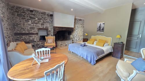 Chambre spacieuse du Manoir de la Bégaudière avec cheminée en pierre, lit, coin salon et table de salle à manger en bois